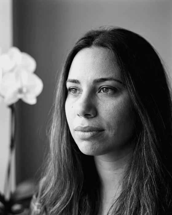 Black and white photograph of the author, looking to the side, with a white orchid beside her